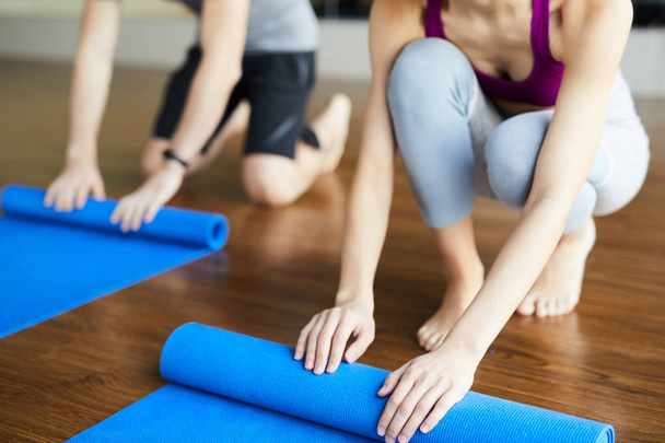 Крупним планом невпізнавані студенти йоги розгортають килимки йоги після практики в студії, приходячи додому
 - Фото, зображення