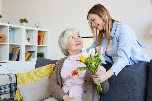 Portrait of young woman giving flowers to elderly mother on Mothers day, copy space - Foto, afbeelding