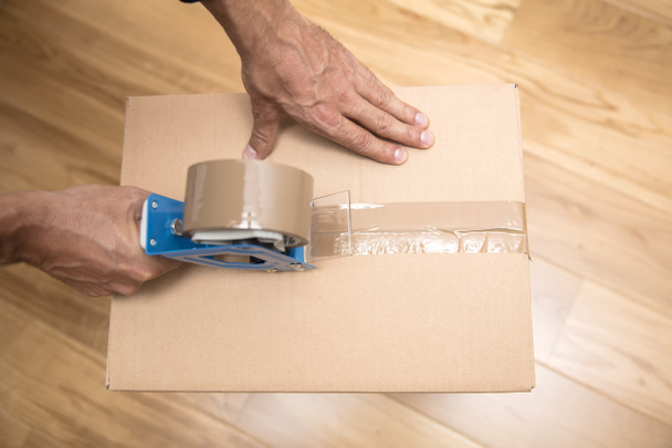 Manos de un hombre usando un dispensador de cinta para sellar una caja de envío
 - Foto, imagen