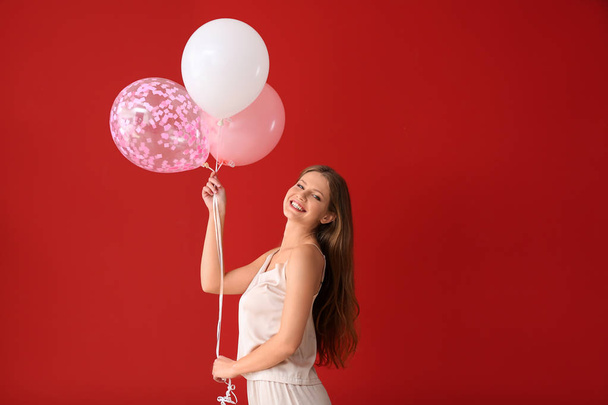 Krásná mladá žena v pyžamu a s vzdušných balonky na barevném pozadí - Fotografie, Obrázek