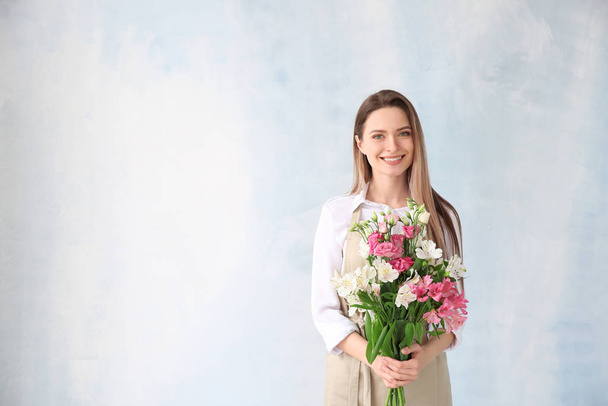 Young female florist with bouquet on color background - Foto, imagen