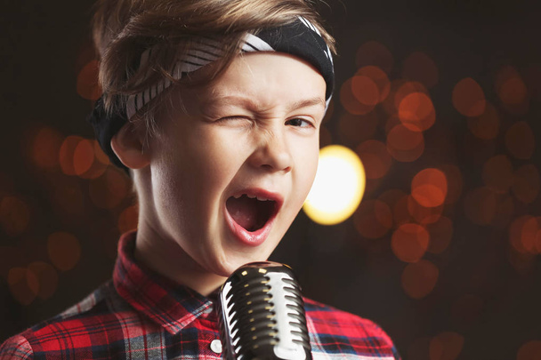 Χαριτωμένο μικρό αγόρι με μικρόφωνο τραγουδώντας ενάντια στο σκοτεινό φόντο - Φωτογραφία, εικόνα