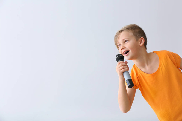 Aranyos kisfiú mikrofonnal a fény hátterében énekel - Fotó, kép