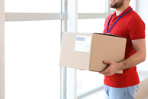 Handsome delivery man with box indoors - Foto, Imagen