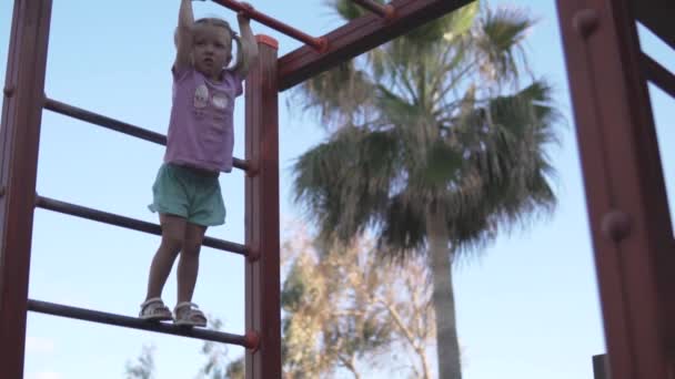 Храбрая маленькая девочка висит на лестнице на детской площадке
 - Кадры, видео