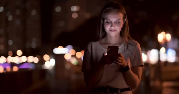 Une jeune fille sur le fond de la ville de nuit regarde dans l'écran du smartphone
 - Séquence, vidéo