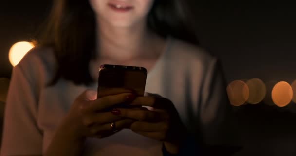 Fiatal lány az éjszakában város szöveges üzeneteket ír egy okostelefonon - Felvétel, videó