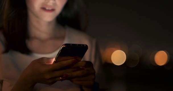 Τη νύχτα, ένα νεαρό κορίτσι κρατά ένα smartphone στα χέρια της και κοιτάζει την οθόνη - Πλάνα, βίντεο