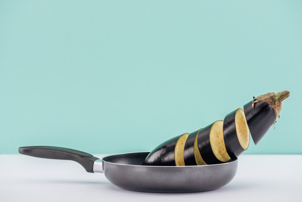 Fresh tasty sliced aubergine in frying pan on white table isolated on turquoise - 写真・画像