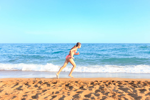 Νεαρή έφηβη τρέχει στην παραλία κατά μήκος της θάλασσας - Φωτογραφία, εικόνα