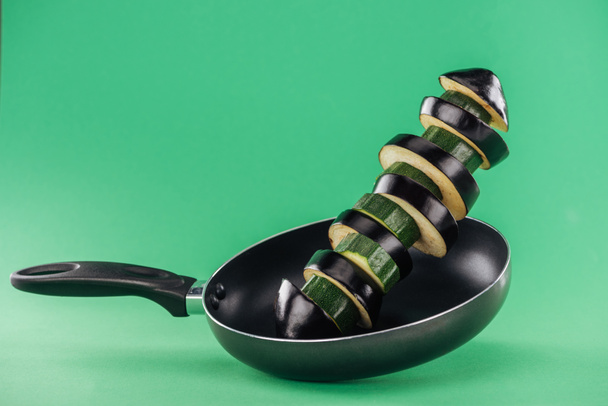 Gesneden groene courgette en aubergine in koekenpan op groene achtergrond - Foto, afbeelding