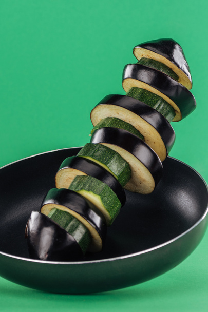 Lähikuva ravitsevaa maukasta tuoretta viipaloitua kesäkurpitsaa ja munakoisoa paistinpannulla vihreällä taustalla
 - Valokuva, kuva