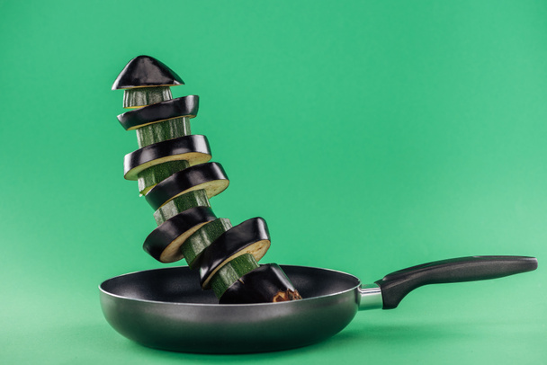 Подрібнені органічні свіжі смачні кабачки та баклажани на сковороді на зеленому фоні
 - Фото, зображення