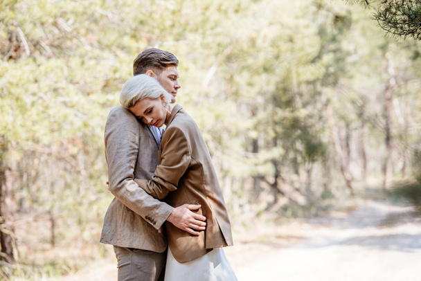 stylish couple in elegant jackets embracing in forest - 写真・画像
