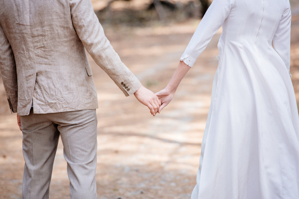 cropped view of just married couple holding hands in forest - Foto, Imagem
