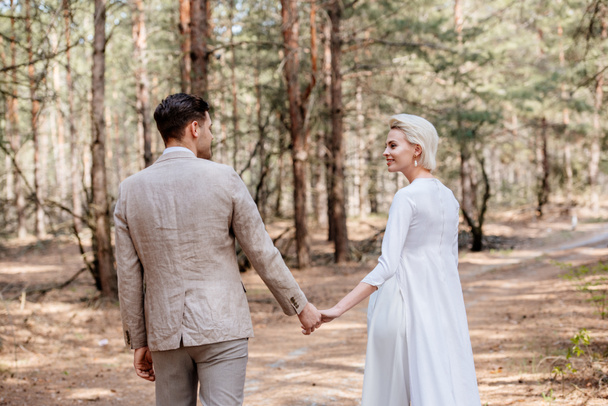 just married couple holding hands and looking at each other in forest - 写真・画像