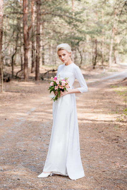 vista a tutta lunghezza della bella sposa che tiene bouquet da sposa nella foresta
 - Foto, immagini