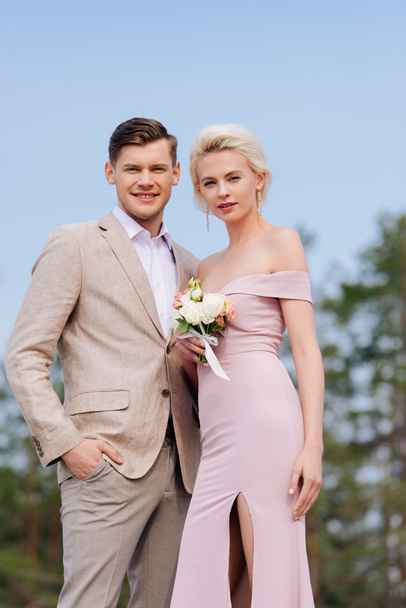 stylish just married couple with wedding bouquet looking at camera - Photo, Image