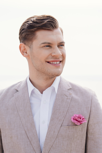 stylish smiling bridegroom in formal wear with boutonniere looking away - Foto, afbeelding