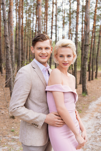 happy just married couple embracing in forest with smile - Фото, изображение
