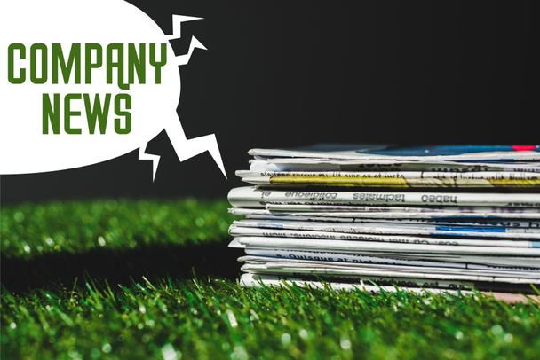 stack of different print newspapers on fresh green grass near speech bubble with company news lettering isolated on black - Photo, Image