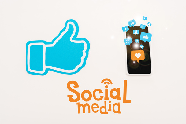 σύμβολο μπλε αντίχειρα κοντά στο smartphone με εικονίδια μέσων κοινωνικής δικτύωσης απομονωμένα σε λευκό - Φωτογραφία, εικόνα