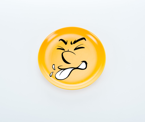 vista superior de la placa de color amarillo brillante con sonrisa disgustada sobre fondo blanco
 - Foto, Imagen