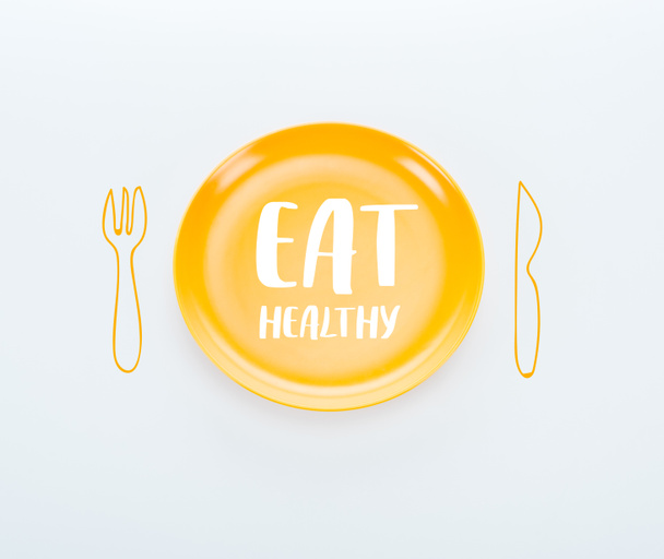 top view of shiny yellow plate with eat healthy lettering and cutlery illustration on white background - Foto, immagini