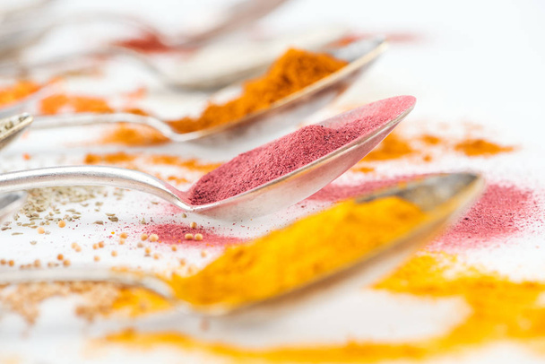 selectieve focus van kleurrijke specerijen in zilveren lepels op witte achtergrond - Foto, afbeelding