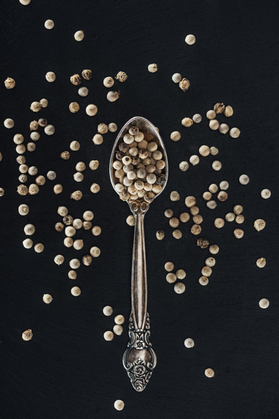 top view of white pepper in silver spoon on black background - Foto, Imagem