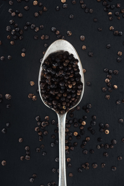 pohled na černou papriku ve stříbrné lžičce na černém pozadí - Fotografie, Obrázek