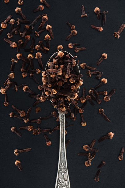 Κορυφαία όψη των σπόρων Γαρύφαλλο σε ασημένιο κουτάλι σε μαύρο φόντο - Φωτογραφία, εικόνα