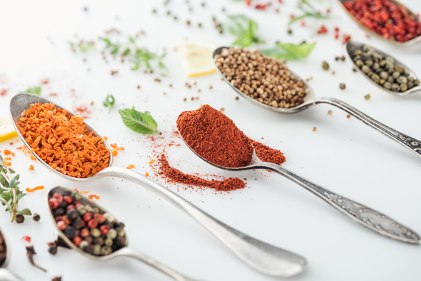 close up view of indian bright spices in silver spoons on white background - Foto, afbeelding