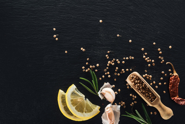 乾燥唐辛子、レモン、ハーブ、ニンニクと黒いテクスチャの背景に木製のへらのコリアンダー種子のトップビュー - 写真・画像