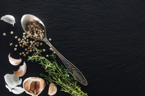 top view of white pepper in silver spoon near garlic cloves and green herb - Photo, Image