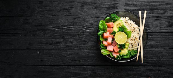 Rice with salmon, avocado and spinach. In a black plate on a wooden background Top view. Free space for your text. Flat lay - Foto, Imagem