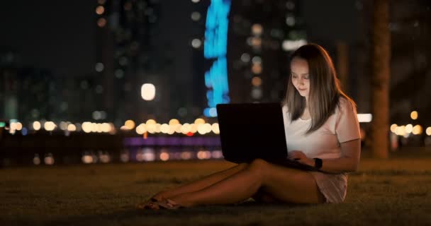 Mujer desarrollador se sienta en el parque por la noche en la ciudad y escribe código mirando la pantalla del ordenador portátil
 - Imágenes, Vídeo