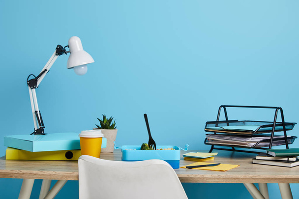 spazio di lavoro con pranzo e caffè in tazza di plastica su tavolo di legno su sfondo blu
 - Foto, immagini