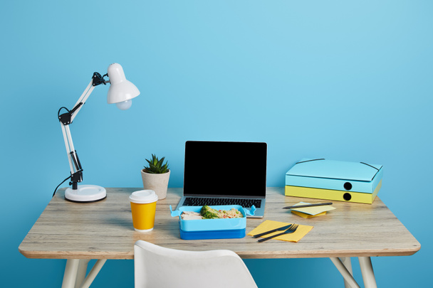 workplace with laptop and lunch box on wooden table on blue background, illustrative editorial - Photo, Image