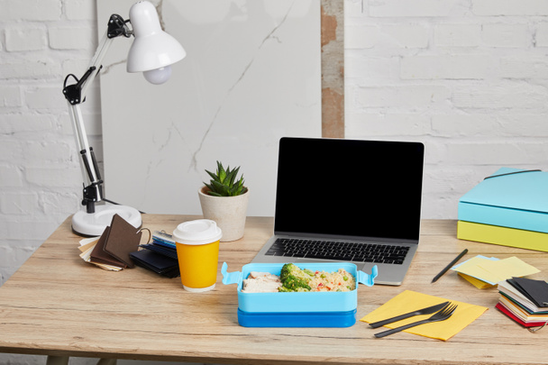Lunchbox mit Reis, Huhn und Brokkoli am Arbeitsplatz mit Laptop auf Holztisch auf weißem Hintergrund, illustrativer Leitartikel - Foto, Bild