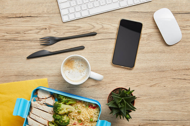 Top uitzicht van lunch box met heerlijke gezonde voeding, warme drank en digitale apparaten op houten tafel - Foto, afbeelding