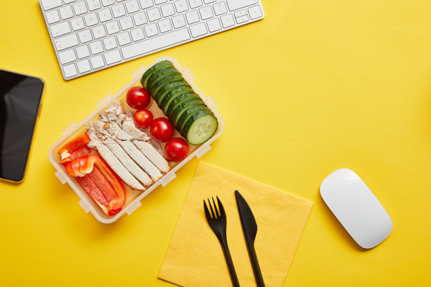 Top view of lunch box with vegetables and chicken on yellow background with computer keyboard - Фото, изображение