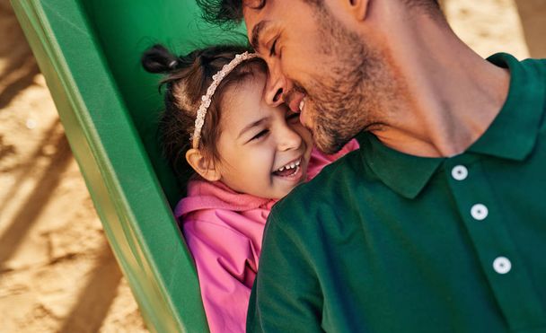 Closeup portrait of happy cute kid daughter smiling and playing with her father outdoors. Handsome dad and toddler little girl having fun and playing at playground. Father and daughter share love - Photo, Image