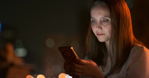 Mujer joven sentada por la noche en la ciudad con smartphone
 - Metraje, vídeo