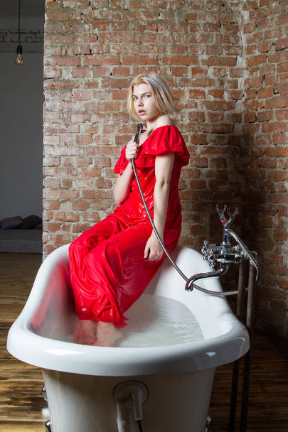 Young girl in a red evening dress sitting in the bathroom - Photo, Image