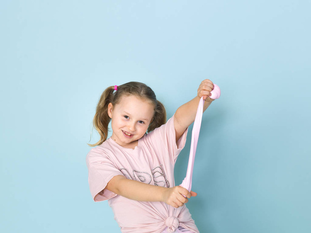 beautiful blonde little girl playing with pink slime in front of blue background - Foto, immagini