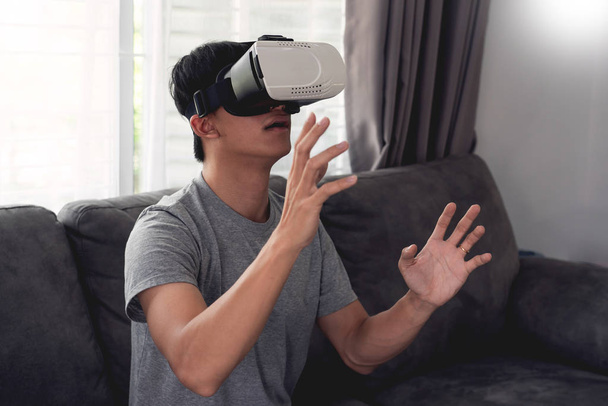 a cheerful man sitting on couch and wearing 3D virtual reality g - Photo, Image