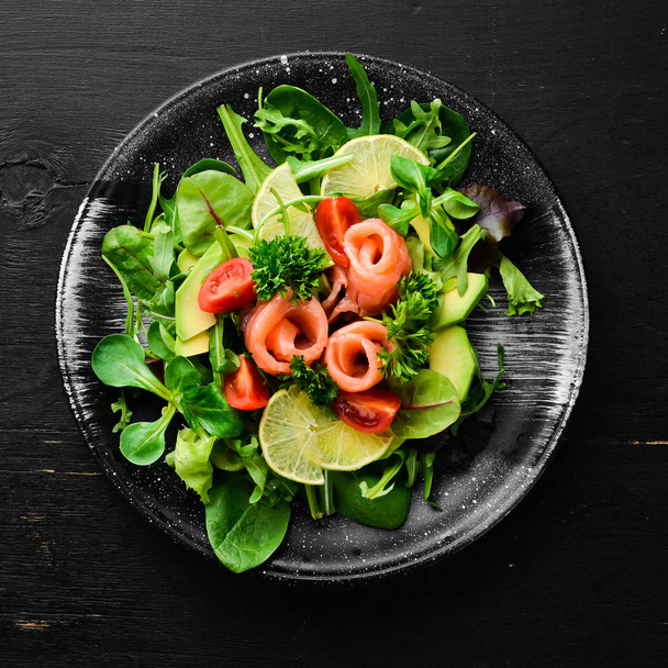Salad with salmon, avocados, tomatoes and spinach. In a black plate on a wooden background Top view. Free space for your text. Flat lay - Fotografie, Obrázek