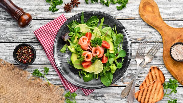 Salad with salmon, avocados, tomatoes and spinach. In a black plate on a wooden background Top view. Free space for your text. Flat lay - Fotoğraf, Görsel