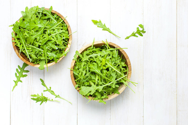 Fresh green arugula leaves on wooden bowl, rucola salad on white wooden rustic background top view with place for text. Rocket salad or arugula, healthy food, diet. Nutrition concept. - Photo, Image